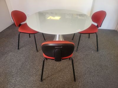 une table en verre entourée de quatre chaises rouges