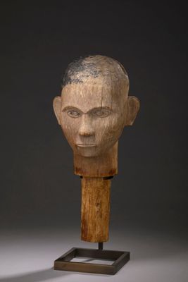 une sculpture en bois représentant une tête d'homme, posée sur un socle