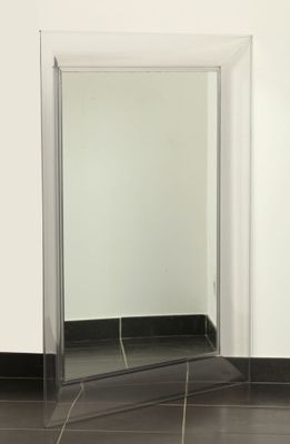 un miroir dans un coin de la salle de bains, dont le sol est carrelé de noir