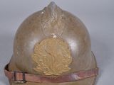 un vieux casque orné d'un emblème doré, posé sur une surface blanche