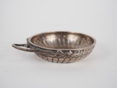 an old silver bowl with a spoon in it on a white surface
