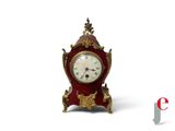 une petite horloge rouge et dorée posée sur une surface blanche