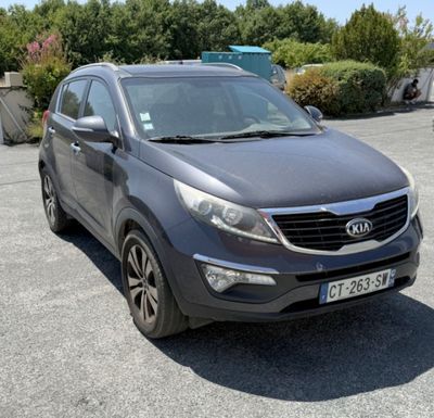 La voiture grise est garée sur le parking, près des buissons.