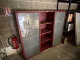 une armoire rouge avec des portes vitrées et un extincteur à l'arrière-plan
