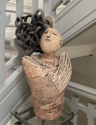 une statue représentant une femme, une fleur dans les cheveux, assise sur une table en verre