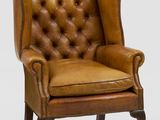a brown leather chair with a buttoned back and wooden legs