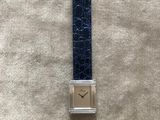 gros plan d'une montre sur une surface blanche avec un bracelet bleu