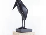 statue d'un oiseau noir posée sur un socle en marbre, sur fond blanc