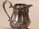 an antique silver pitcher with a handle on a white surface