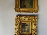Deux tableaux dans des cadres dorés sont accrochés à un mur blanc dans une pièce