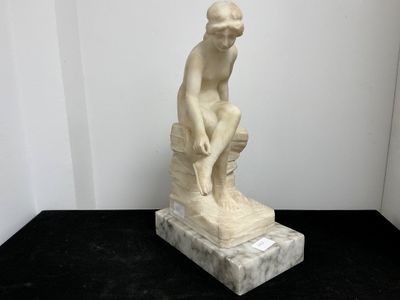 statue en marbre représentant un homme assis sur un rocher, posée sur un socle noir