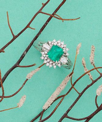 une bague sertie d'une émeraude et de diamants, posée sur une branche d'arbre