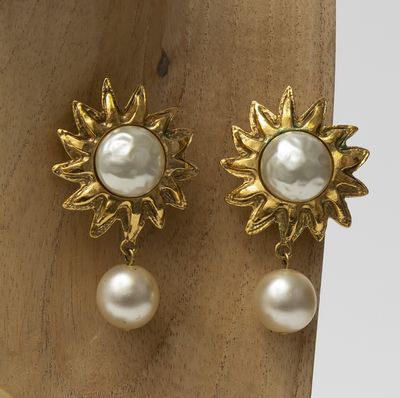 pair of pearl and gold sunburst earrings on a wooden stand