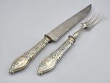 une paire de couteaux plaqués argent et un couteau posés sur une surface blanche