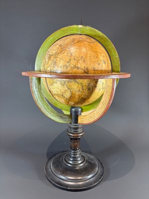 un vieux globe terrestre posé sur un socle en bois, sur fond gris