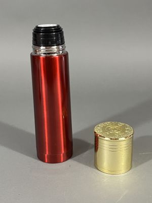 une bouteille rouge et dorée à côté d'une pièce d'or