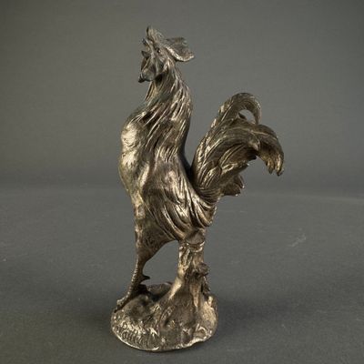 a silver statue of a rooster on a gray surface