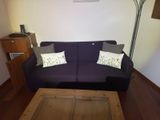 a purple couch with two pillows and a coffee table in the corner
