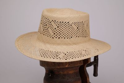 chapeau de paille beige posé sur un support en bois, sur fond gris
