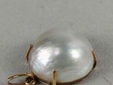 a close up of a white pearl pendant on a gold plated chain