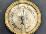 an antique brass barometer with thermometer on a black surface