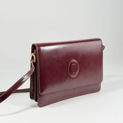 Ce sac à main en cuir marron est muni d'une longue bandoulière et d'une fermeture à fermoir.
