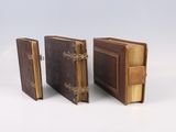 trois livres reliés en cuir, empilés les uns sur les autres sur une surface blanche