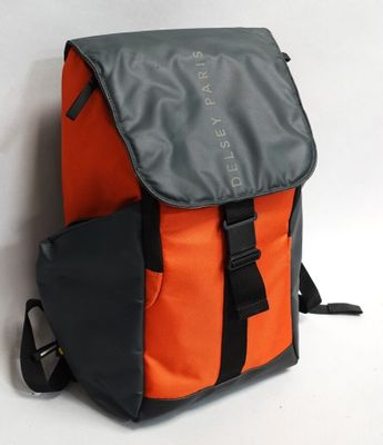 un sac à dos orange et gris posé contre un mur, sur une surface blanche