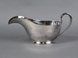 a silver sauce boat with a curved handle on a gray surface