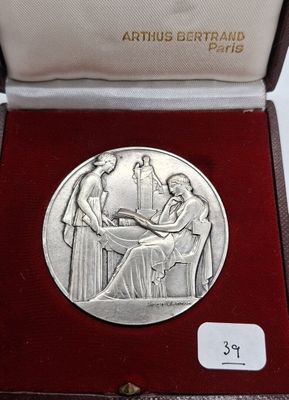 une image représentant une médaille d'argent dans un coffret rouge orné de la photo d'une femme assise à une table