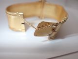 a gold bracelet with a chain on it on a white surface