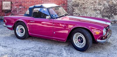a pink convertible car parked in front of a brick wall