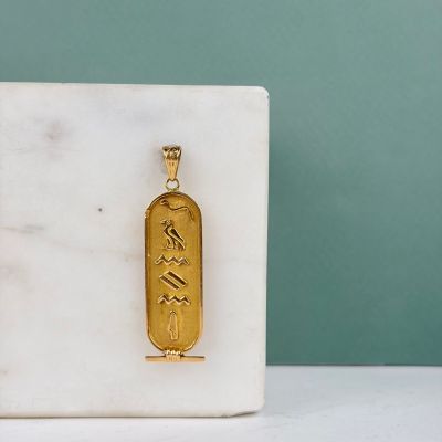une photo d'un pendentif plaqué or posé sur un bloc de marbre