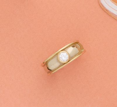 un gros plan d'une bague en or sertie d'un diamant, posée sur un fond rose
