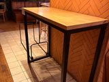 a long table with two stools next to a brick wall