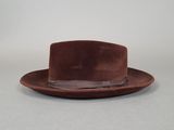 Le chapeau est marron et est orné d'une plume sur le dessus.