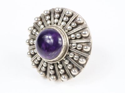 une image représentant une bague en argent ornée d'une pierre violette au centre
