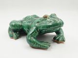 une figurine de grenouille verte posée sur une surface blanche