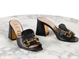 une paire de mules en cuir noir ornées d'une boucle dorée au talon