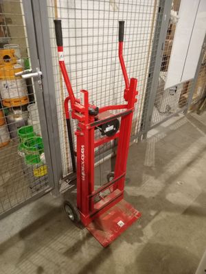 a red hand truck that is sitting in front of a fence