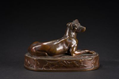 bronze statue of a dog laying down on a base on a black background