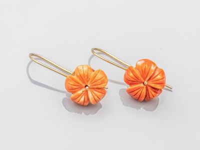 une photo représentant une paire de boucles d'oreilles orange posées sur une surface blanche