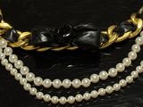 two strands of pearls and a gold chain necklace on a black surface