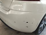 the rear end of a white car with a dent in it