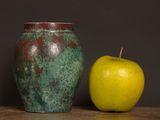 a green apple next to a brown vase on a table