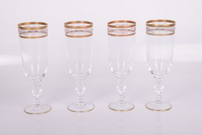 quatre verres à vin à bord doré posés sur une surface blanche