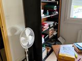 a desk with a fan and a bookcase in the corner