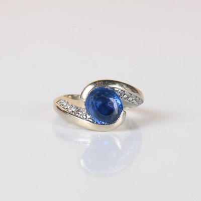 une photo d'une bague sertie d'un saphir bleu et de diamants, posée sur une surface blanche