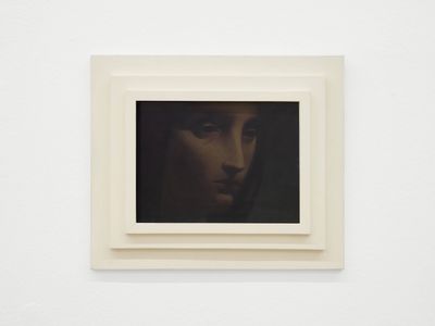 painting of a woman ' s face in a white frame on a white wall