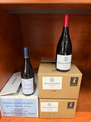 deux bouteilles de vin posées sur des cartons, sur une étagère en bois